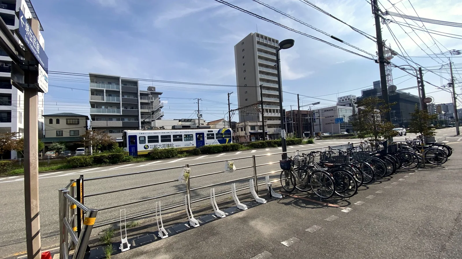 A Hankai Tramway streetcar passing on the street near the Sakai Traditional Crafts Museum, with a direction sign in the foreground