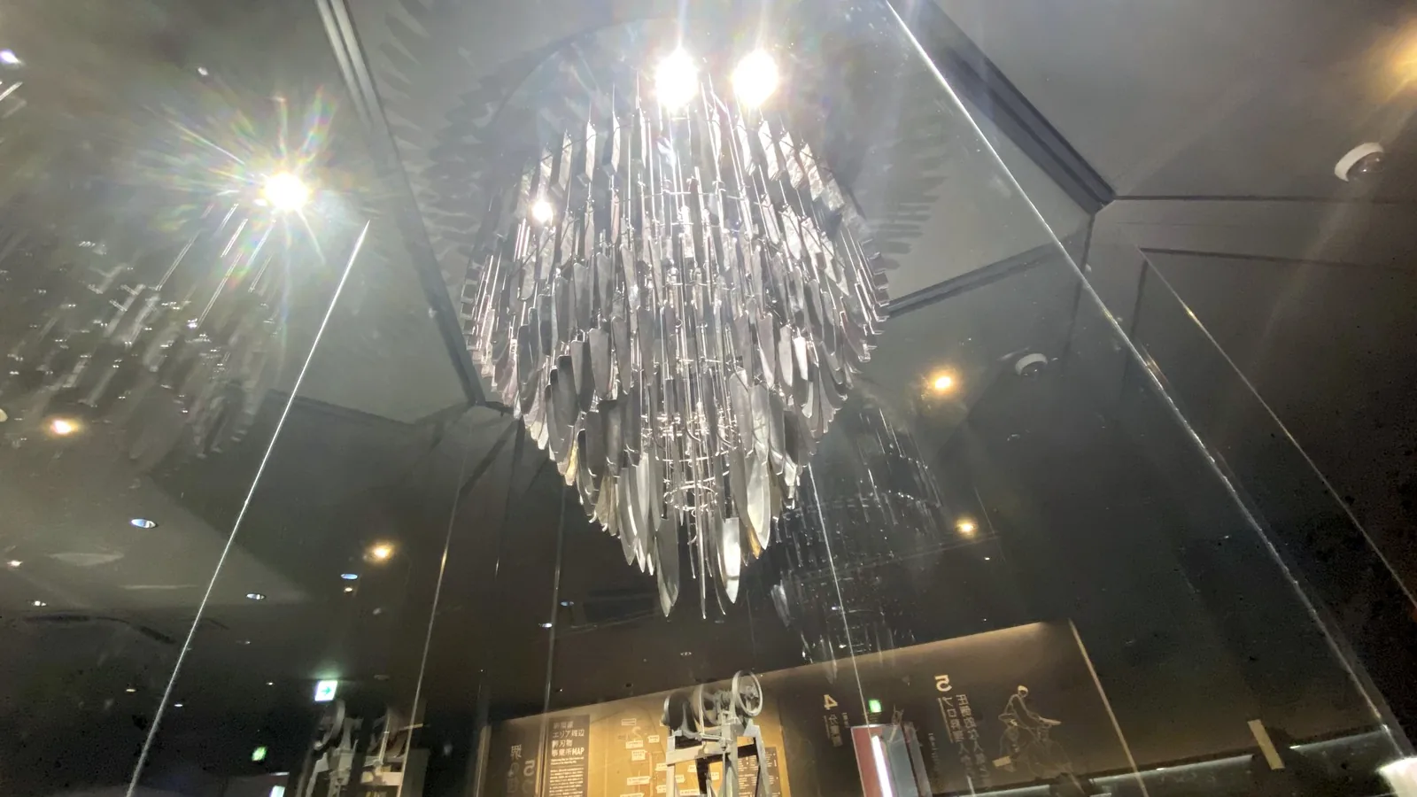 HIBANA lit by ceiling spotlights, with light flare and reflections on the glass enclosure