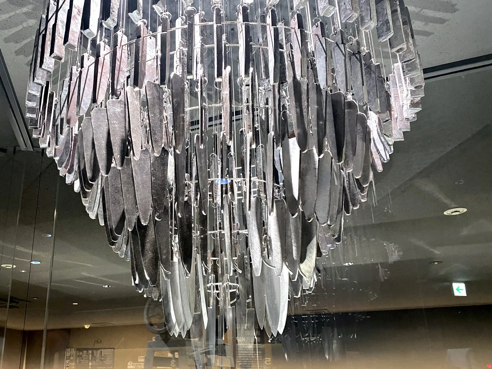 Close view from below of the HIBANA chandelier, with rough steel pieces in the upper tiers and polished knife blades in the lower tiers