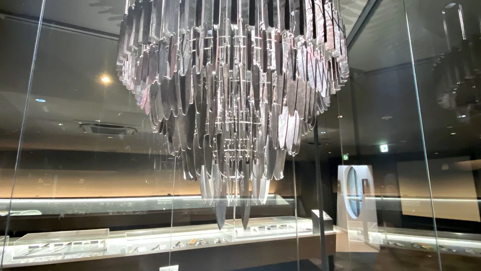 The HIBANA knife chandelier seen from the exhibition floor, with display cases below it
