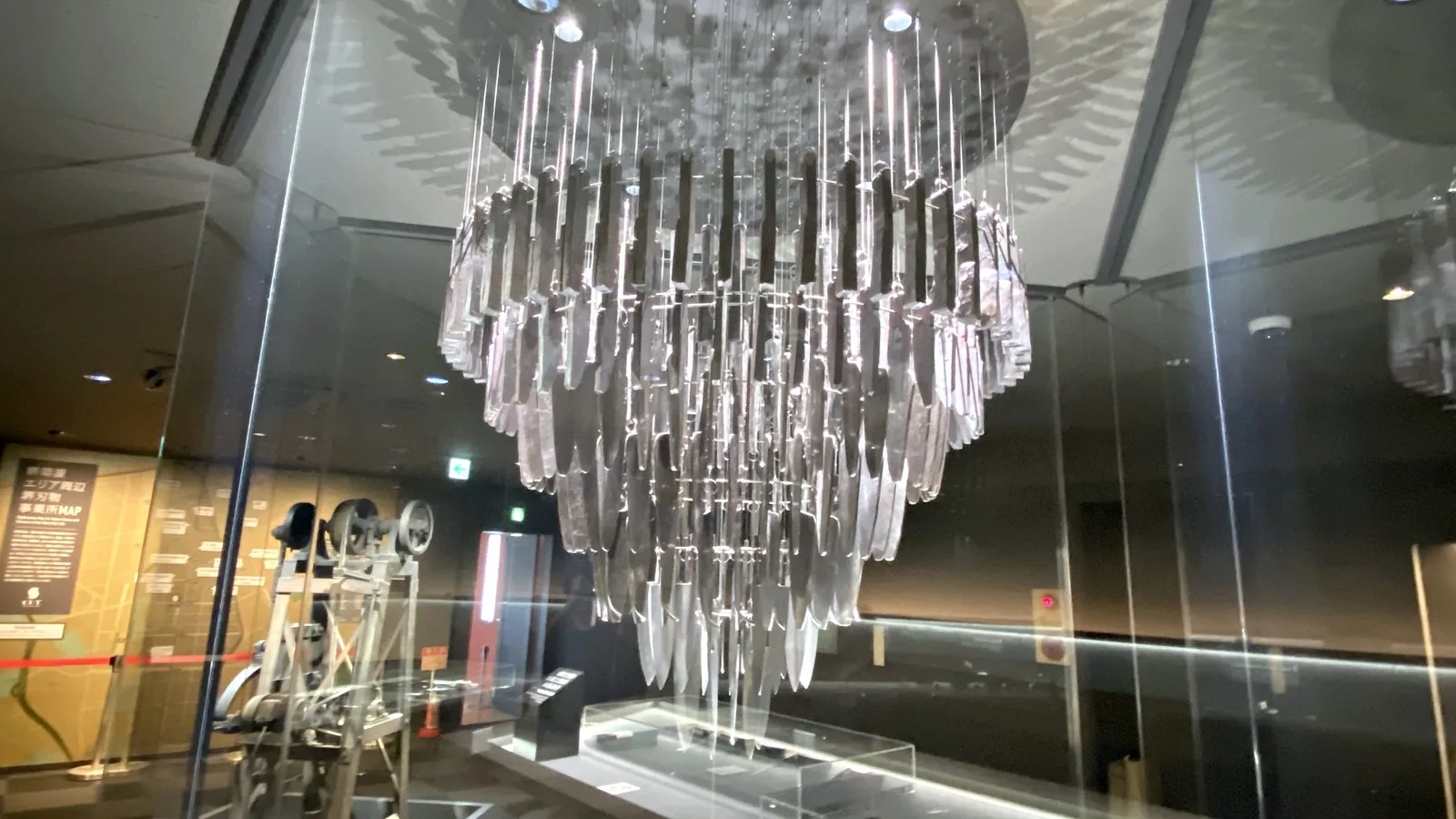 The HIBANA chandelier at Sakai Knife Museum CUT, a tiered chandelier of knife blanks and blades hanging inside a glass enclosure