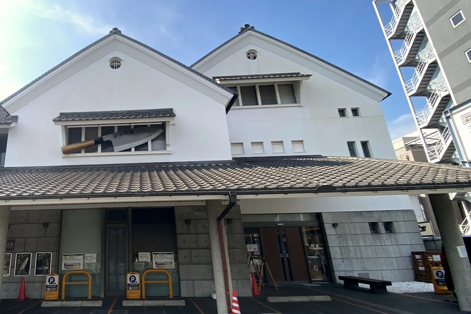 Exterior of the Sakai Traditional Crafts Museum in Sakai, Osaka: a white storehouse-style building with a tiled roof and a large kitchen knife displayed in the upper window
