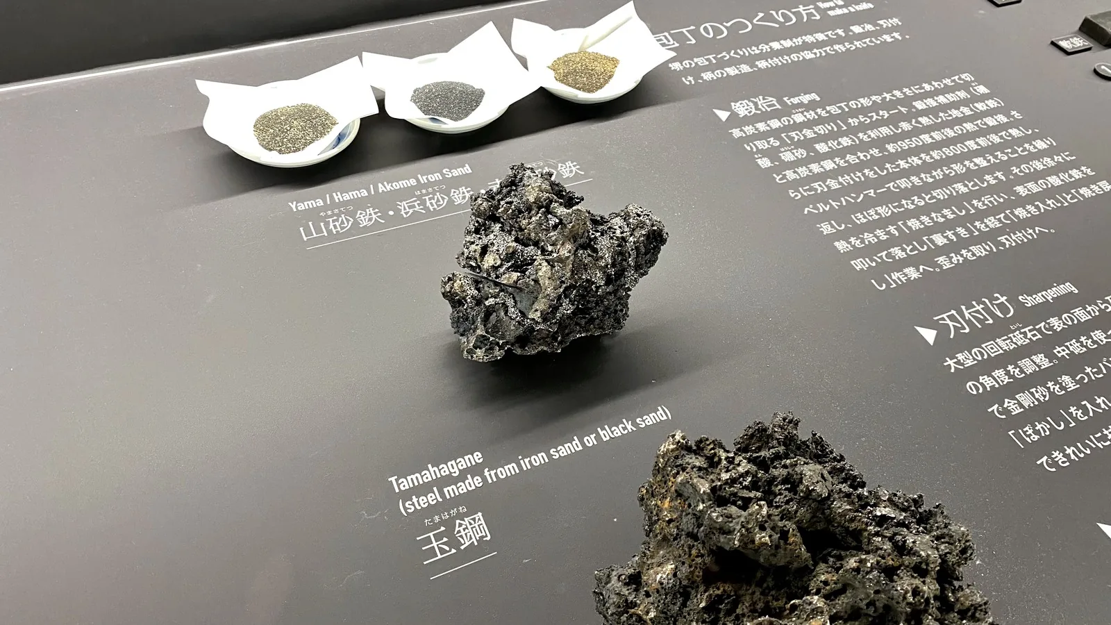 Iron sand samples and lumps of tamahagane steel displayed as knife-making raw materials