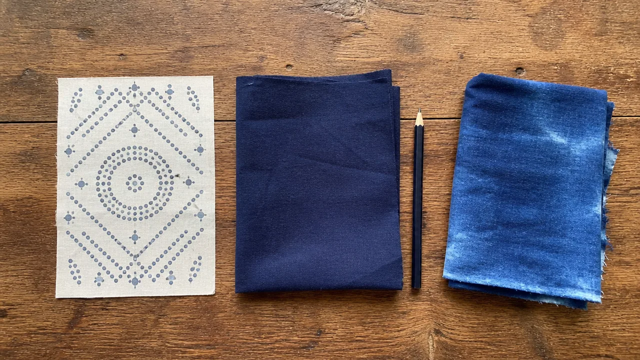 A white cloth printed with a dotted pattern, folded navy fabric, a pencil and folded light-blue dyed fabric