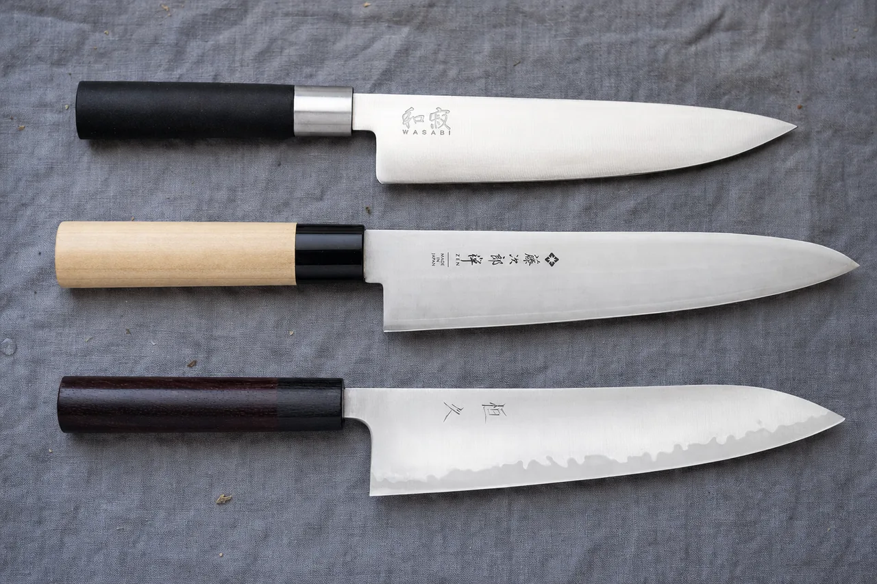 Three gyuto knives: Kai Wasabi with a black handle, Tojiro Zen with a magnolia handle, and Tsunehisa with a dark octagonal handle