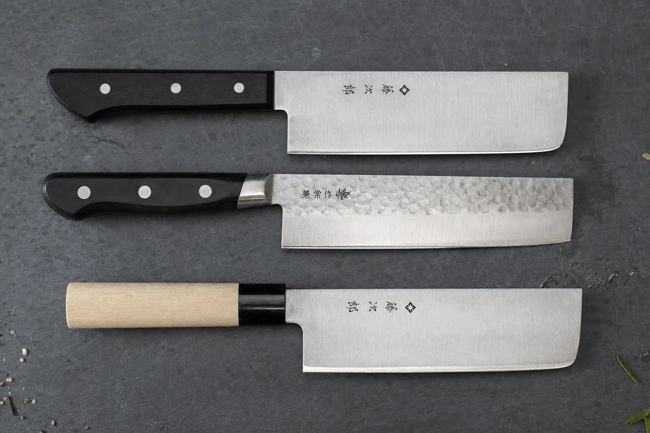 Three nakiri knives on slate: Tojiro Basic, hammered Kanetsune KC-923, and Tojiro Zen with a magnolia handle