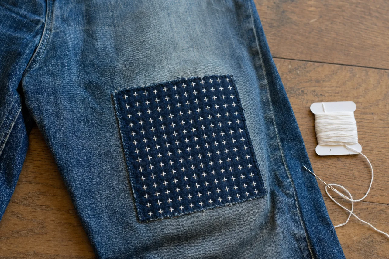 Blue jeans mended with an indigo patch stitched in a white juji (cross) sashiko pattern