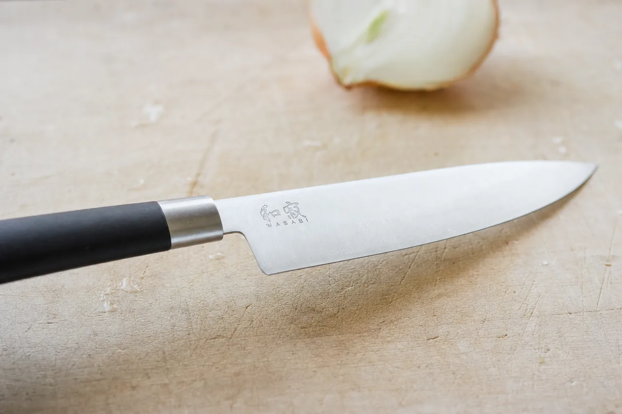 Close-up of a Kai Wasabi gyuto blade and black handle on a maple cutting board