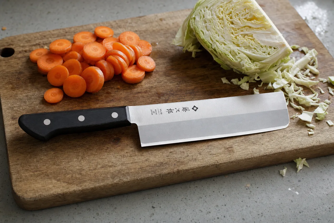 Tojiro Basic nakiri with a black three-rivet handle beside sliced carrots and cabbage on a wooden cutting board
