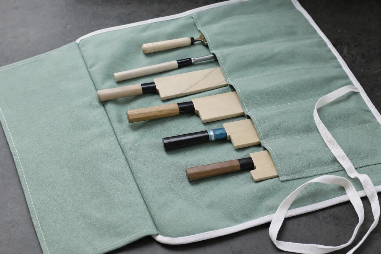 Open grey-green cotton knife pouch with six pockets holding sheathed Japanese knives