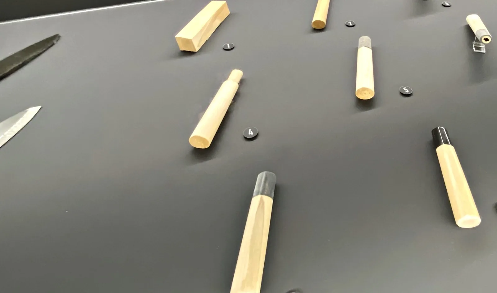 Display of wooden knife handles at different stages of shaping, next to unfinished blades