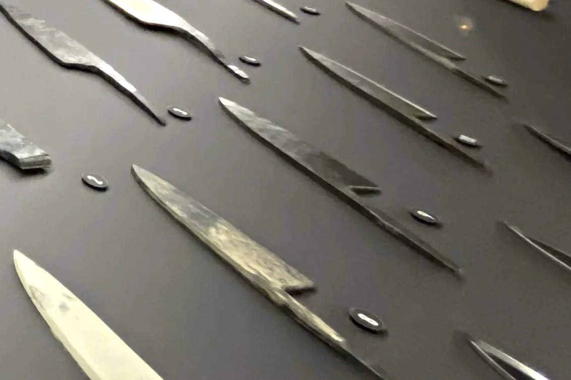 Long display showing how a kitchen knife is made, with process photos above and knife blanks at each stage laid out below